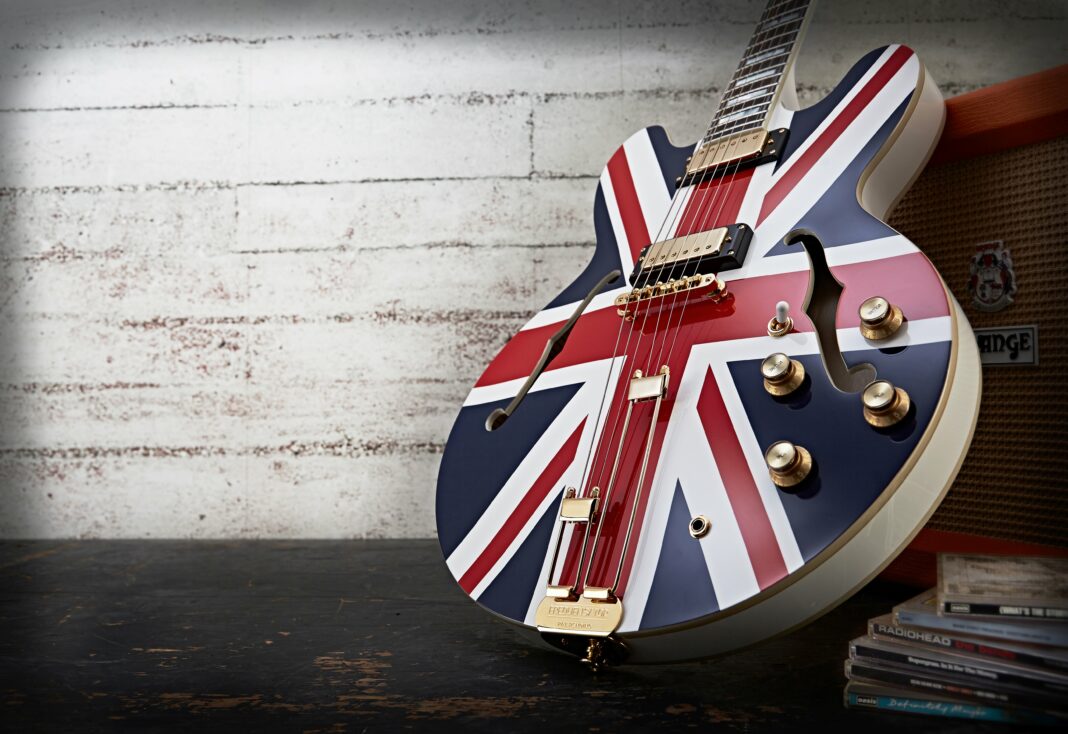 Eine Gitarre, auf die eine Großbritannien-Flagge lackiert ist, lehnt vor einer weiß getünchten Ziegelwand an einem Gitarrenverstärker.