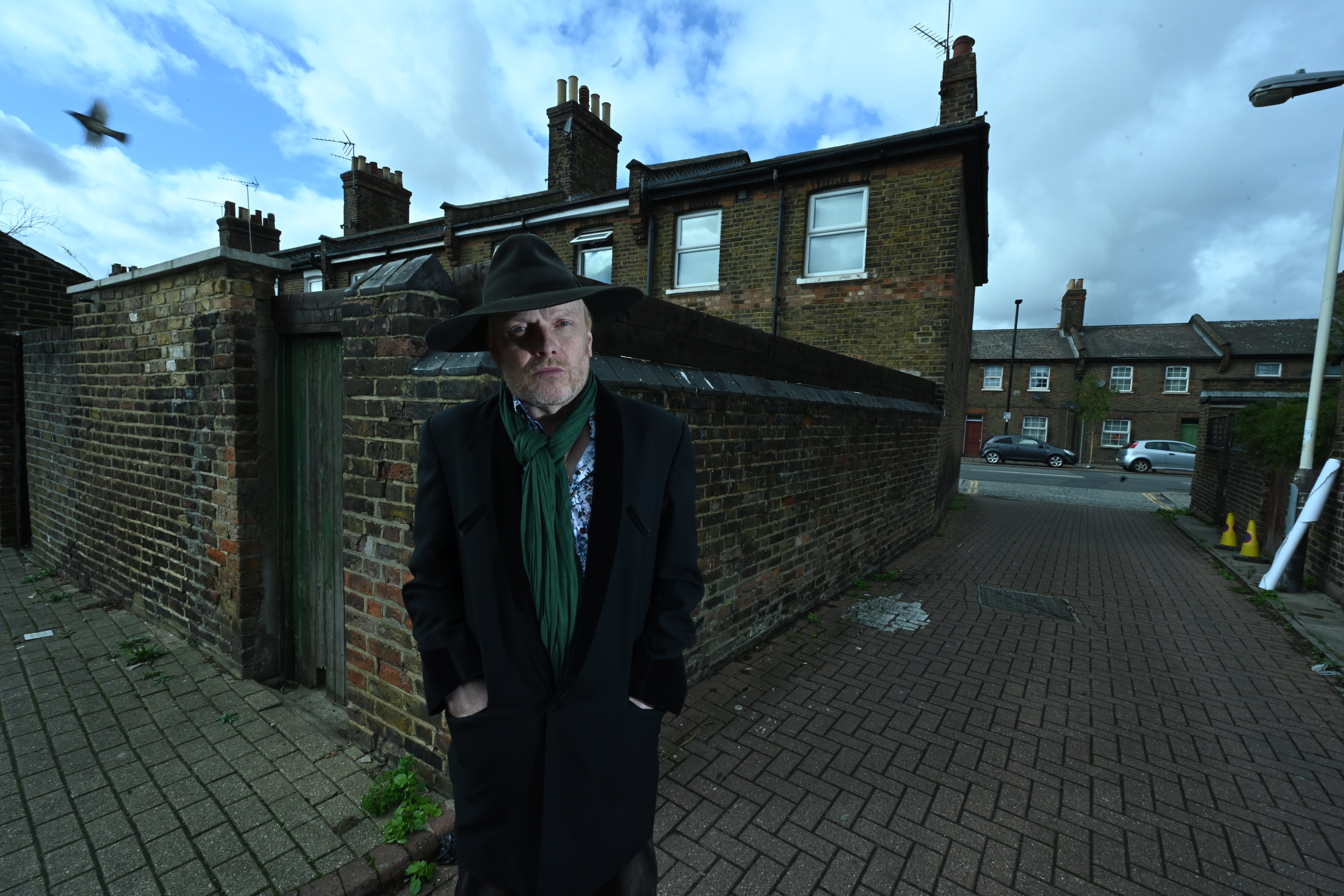 Luke Haines steht im Hinterhof von typischen kleinen Stadthäusern aus Ziegeln irgendwo in England.